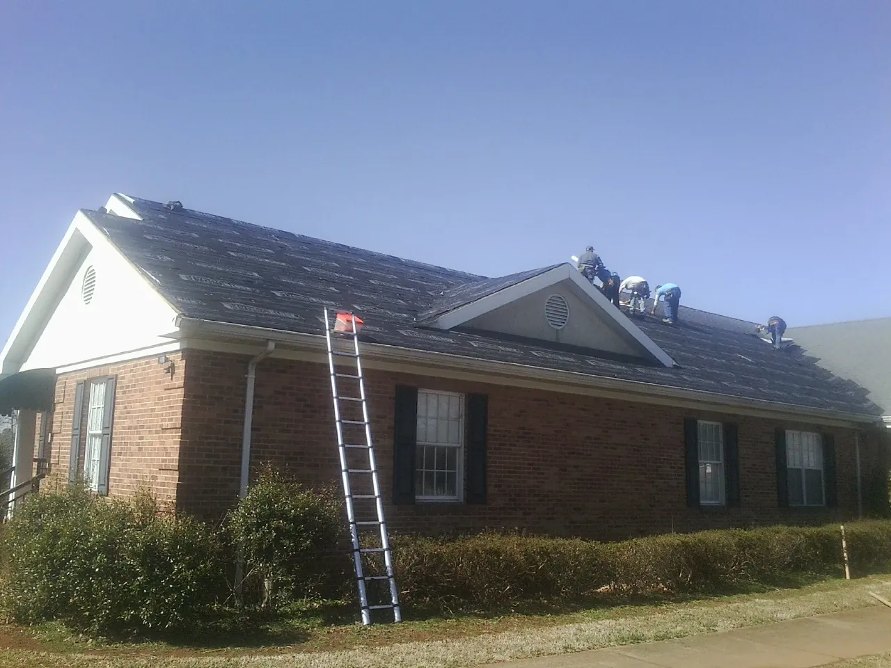 Crew tearing shingles off a brick ranch roof with a ladder set — Metal Roof Repair work by our crew in Rome