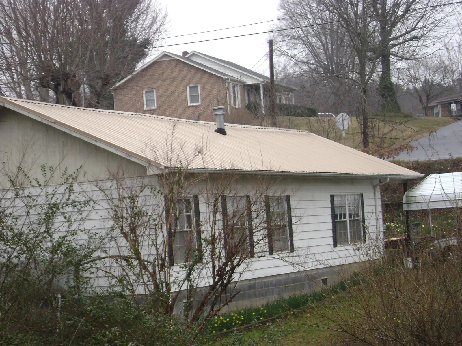 Tan metal roof on a white sided house set into a hillside — Commercial Roofing by Roofing Brothers in Rome