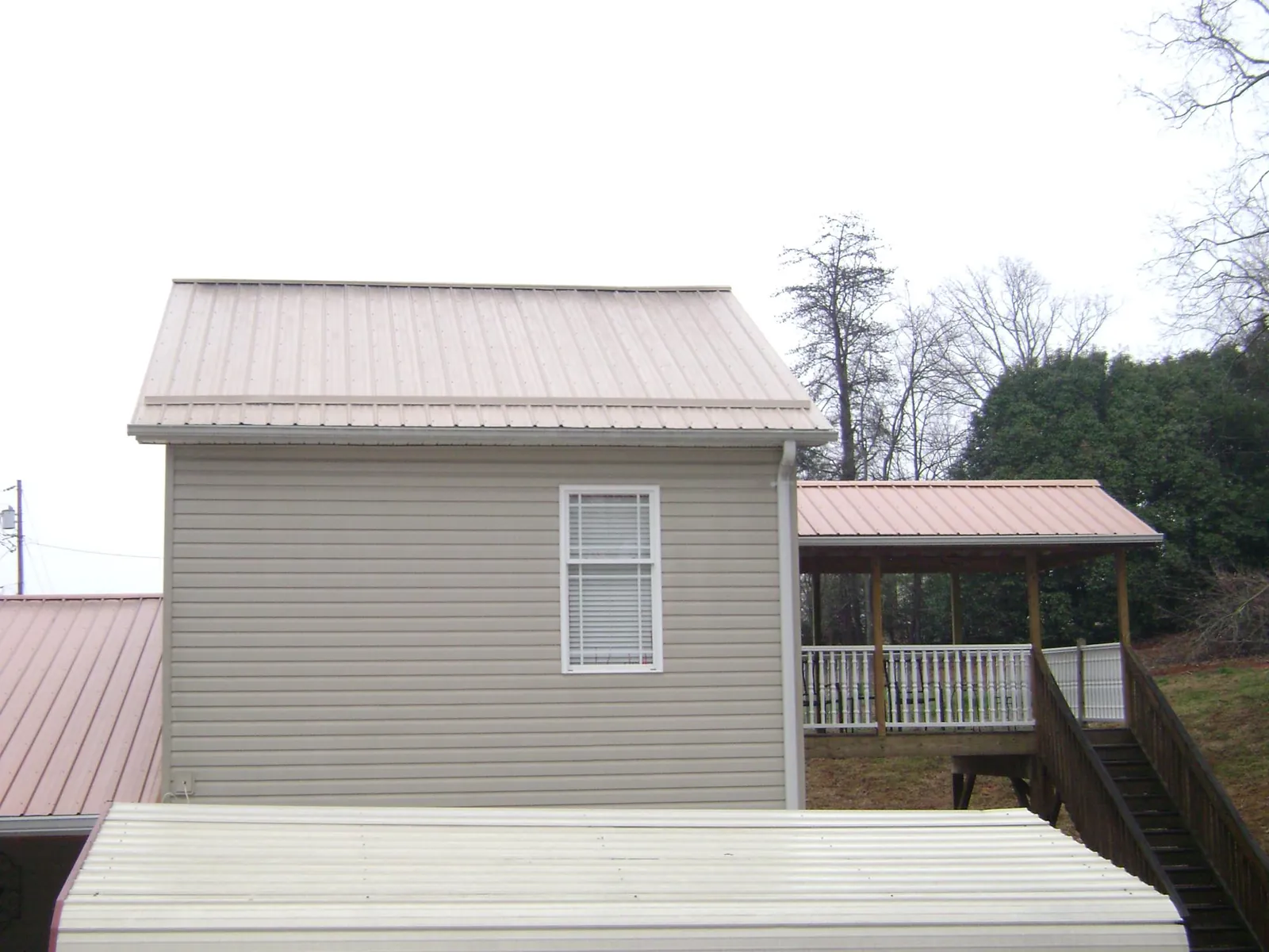 Tan metal roofs on a two story addition and attached porch, from a Roof Replacement job in Rome